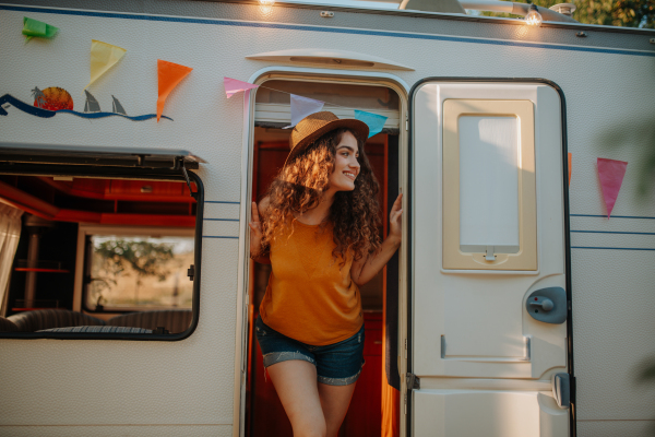 Young woman is on a camping trip in nature, standing on caravan steps. Caravan traveling for young people