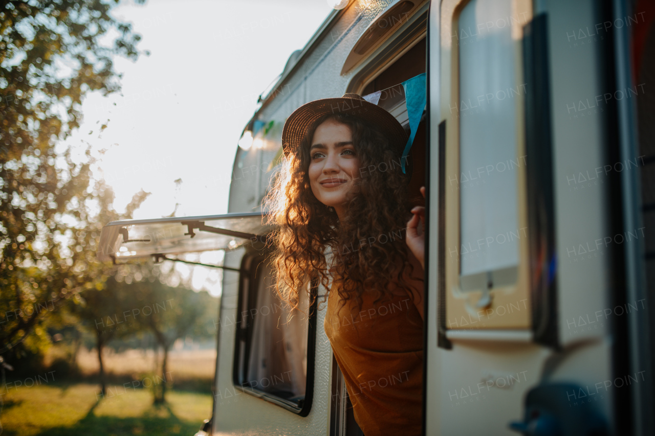 Young woman is on a camping trip in nature, standing on caravan steps. Caravan traveling for young people