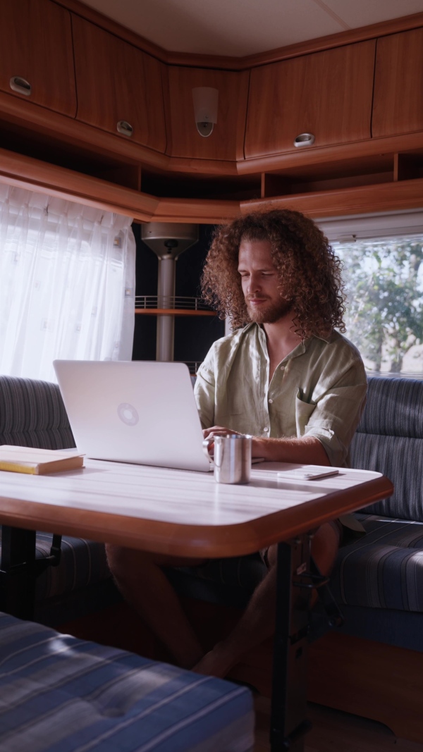 Young man sitting inside of a caravan and working on his laptop. Concept of remote work.