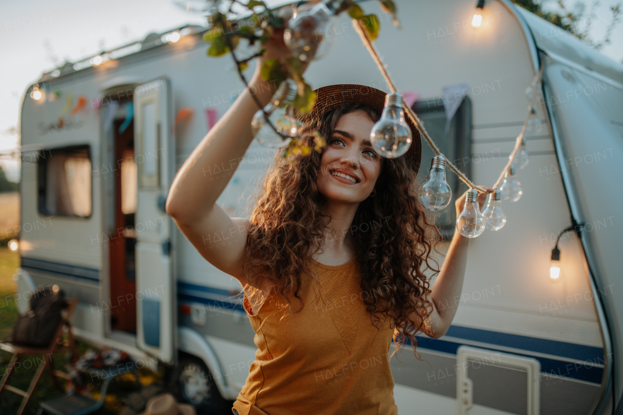 Young beautiful woman is on a camping trip in nature, putting lights on tree, preparing for evening