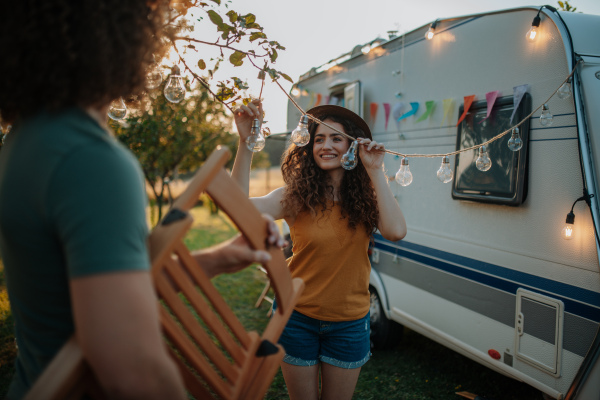 Young beautiful woman is on a camping trip in nature, putting lights on tree, preparing for evening