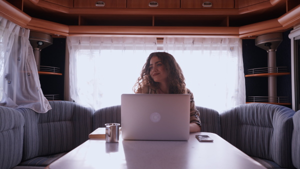 Young woman sitting inside of a caravan and working on her laptop. Concept of remote work.