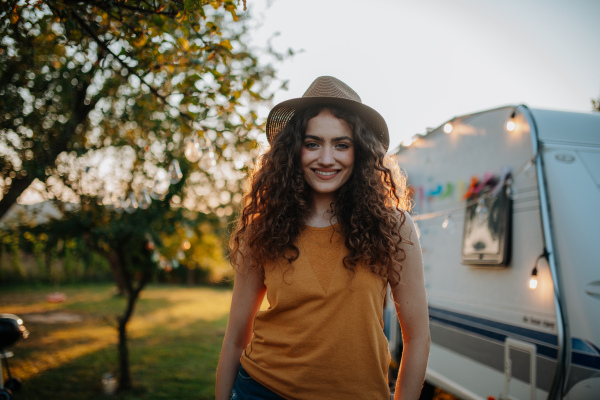 Portrait of young beautiful woman on camping trip in nature, standing in front of caravan