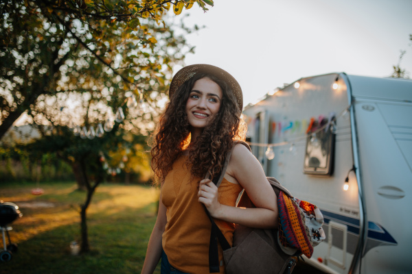 Portrait of young beautiful woman on camping trip in nature, standing in front of caravan