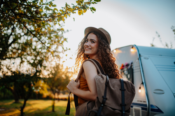 Portrait of young beautiful woman on camping trip in nature, standing in front of caravan