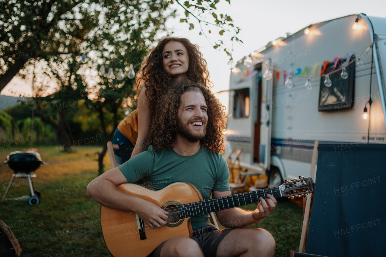 Couple sitting by campfire in the evening, enjoying peaceful moment. Man playing guitar and singing song to his girlfriend.