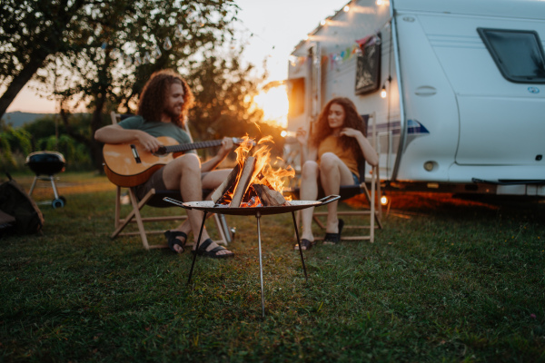 Couple sitting by campfire in the evening, enjoying peaceful moment. Man playing guitar and singing song to his girlfriend.