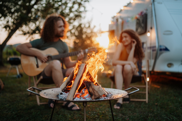 Couple sitting by campfire in the evening, enjoying peaceful moment. Man playing guitar and singing song to his girlfriend.