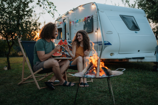 Couple having romantic picnic during camping trip in nature, eating watermelon. Caravan traveling for young people