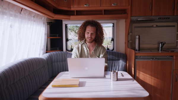 Young man sitting inside of a caravan and working on his laptop. Concept of remote work.