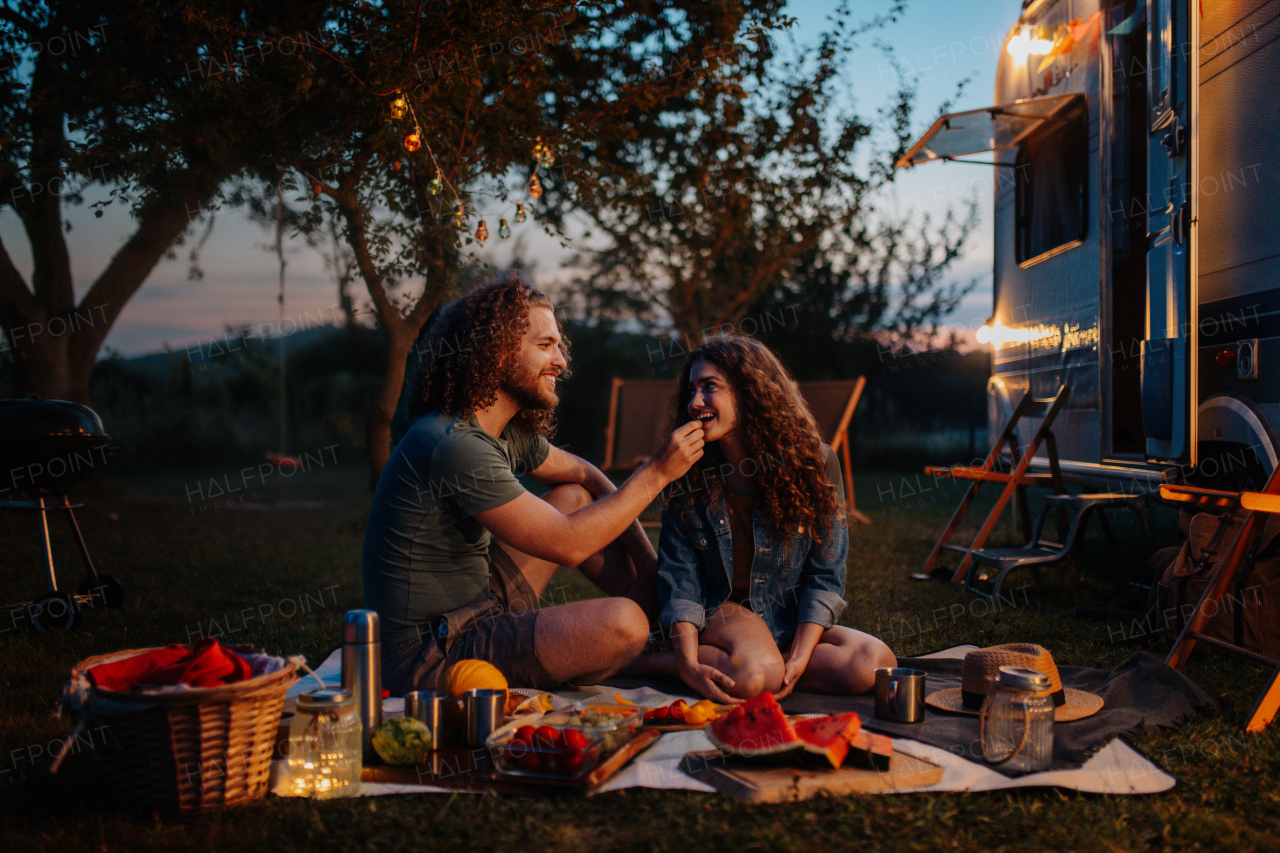 Couple having romantic picnic during camping trip in nature. Man feeding his girlfriend. Caravan traveling for young people