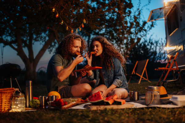 Couple having romantic picnic during camping trip in nature. Caravan traveling for young people