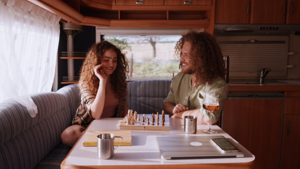 Young couple in love on a roadtrip with a caravan, camping and exploring new places. Sitting inside and playing chess.