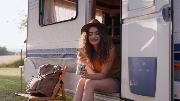 Young woman sitting inside of a caravan and scrolling her smartphone.