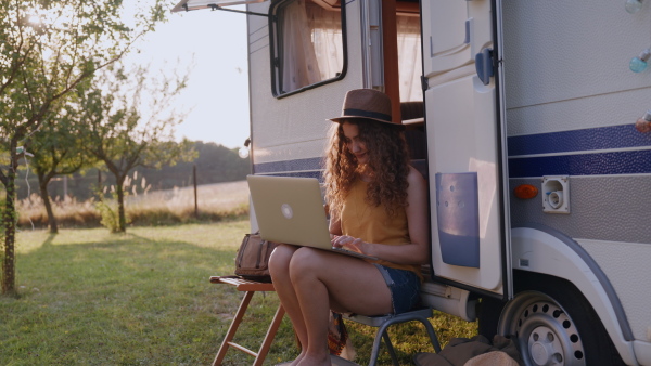 Young woman sitting in front of a caravan and working on her laptop. Concept of remote work.