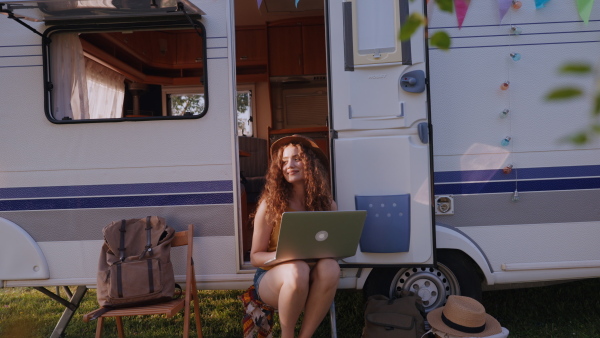 Young woman sitting in front of a caravan and working on her laptop. Concept of remote work.