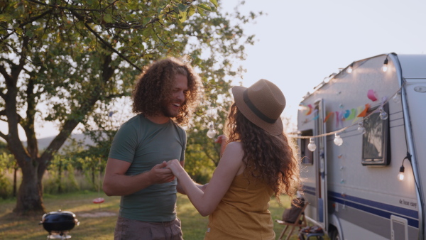 Young couple in love on a roadtrip with a caravan, camping and exploring new places. Dancing during a sunset.