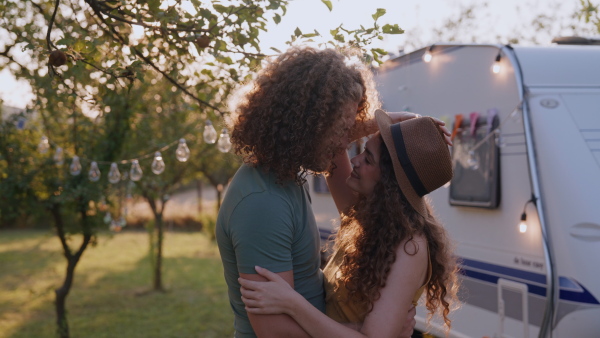 Young couple in love on a roadtrip with a caravan, camping and exploring new places. Dancing during a sunset.