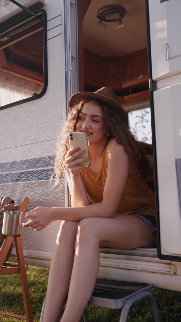 Young woman sitting inside of a caravan and scrolling her smartphone.