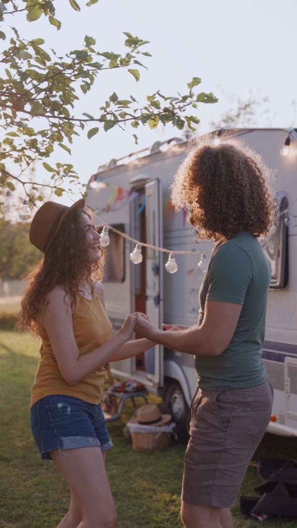 Young couple in love on a roadtrip with a caravan, camping and exploring new places. Dancing during a sunset.