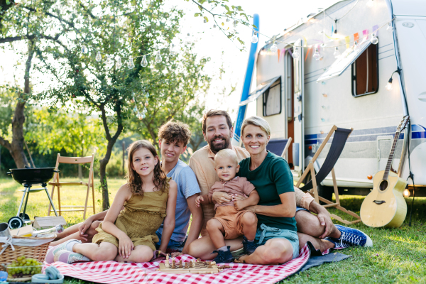 Family having picnic in front of caravan, sitting on picnic blanket. Family trip in caravan.