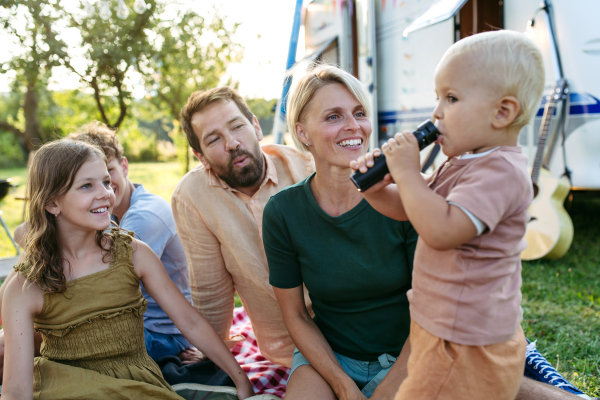 Family having picnic in front of caravan, sitting on picnic blanket. Family trip in caravan.