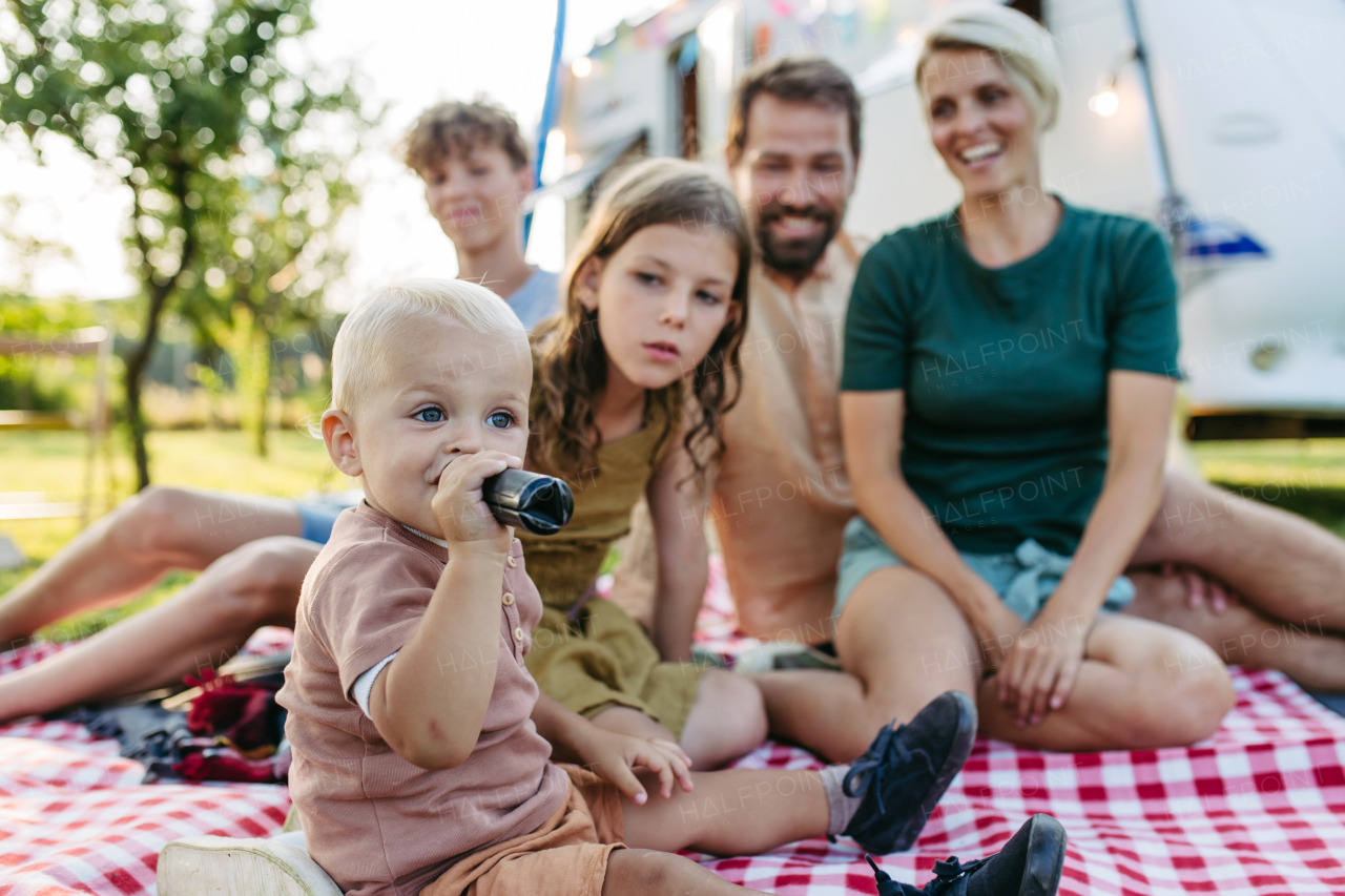 Family having picnic in front of caravan, sitting on picnic blanket. Family trip in caravan.