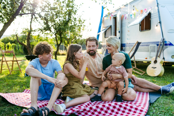 Family having picnic in front of caravan, sitting on picnic blanket and blowing bubbles. Family trip in caravan