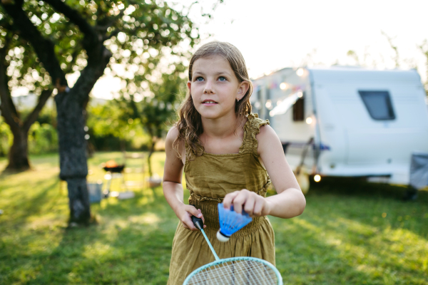 Playing badminton outside on the lawn in the garden. The girl is holding a racket and a shuttlecock, preparing to serve.