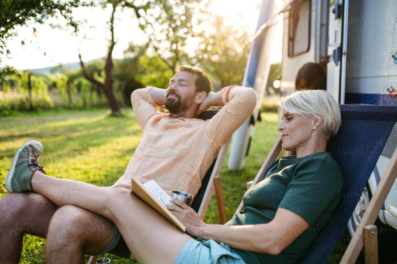 Parents relaxing in front of caravan during their low-cost camping trip. Family roadtrip in caravan.