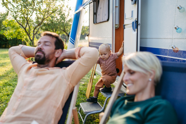 Parents relaxing in front of caravan during their low-cost camping trip. Family roadtrip in caravan.