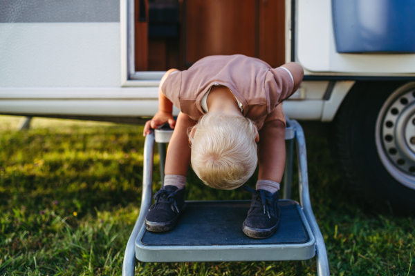 Little boy is sitting on the caravan steps, looking between his legs at what is behind him.