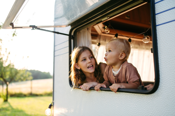 Big sister and small toddler brother are standing in the caravan, looking out the window.