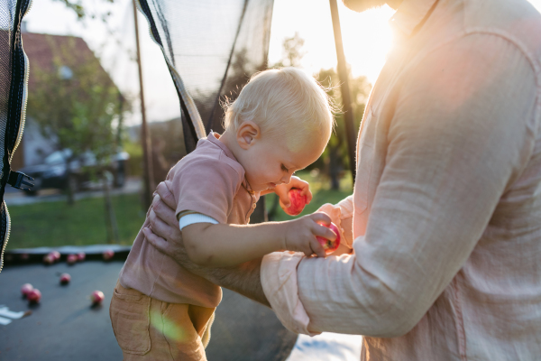 Dad is helping his toddler son play on the trampoline.