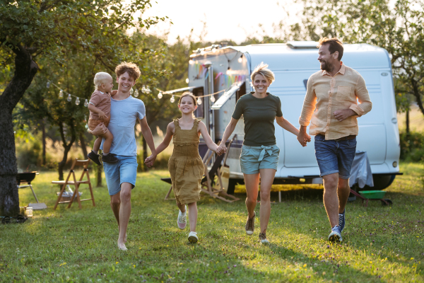 Portrait of family members walking in front of caravan and holding hands. Family roadtrip in caravan.