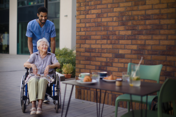 Caregiver taking his senior client on wheelchair at breakfast outdoor in the city.