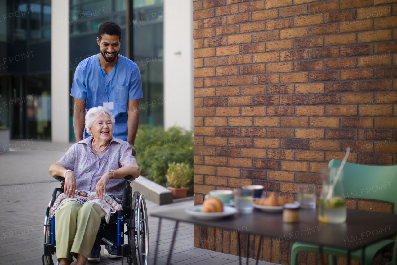 Caregiver taking his senior client on wheelchair at breakfast outdoor in the city.