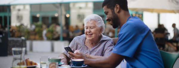 Caregiver having coffee with his client and learning her using a smartphone, outdoor at cafe.