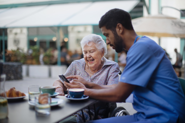 Caregiver having coffee with his client and learning her using a smartphone, outdoor at cafe.