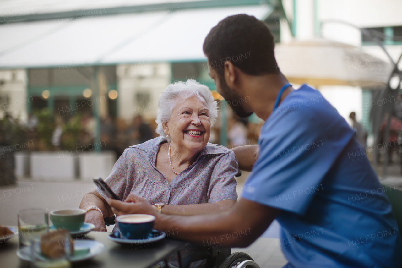 Caregiver having coffee with his client and learning her using a smartphone, outdoor at cafe.