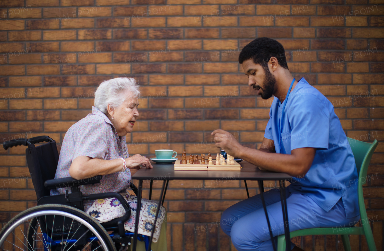 Caregiver playing chess and drinking coffe with his client outdoor at a cafe.