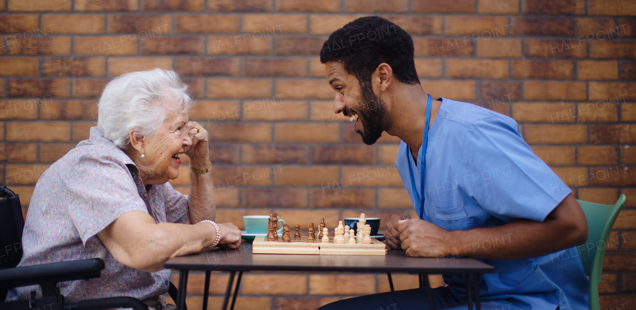 Caregiver playing chess and drinking coffe with his client outdoor at a cafe.