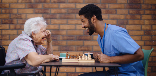 Caregiver playing chess and drinking coffe with his client outdoor at a cafe.