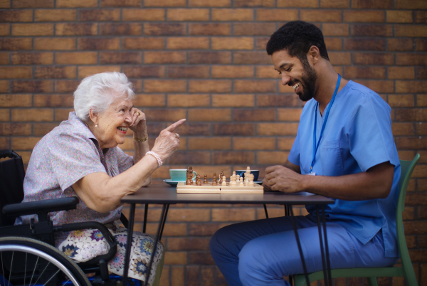 Caregiver playing chess and drinking coffe with his client outdoor at a cafe.