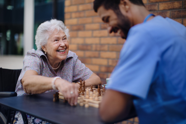 Caregiver playing chess and drinking coffe with his client outdoor at a cafe.