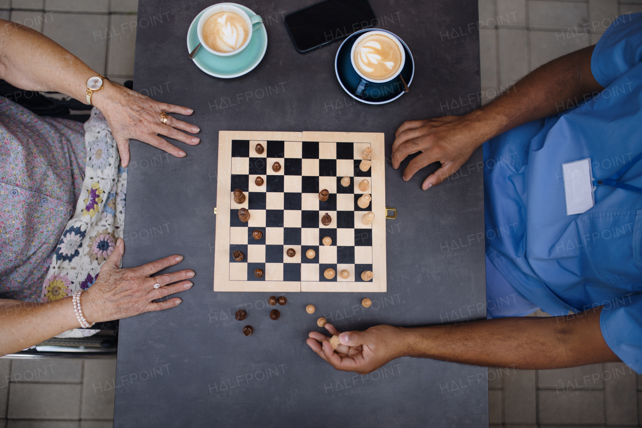 Top view of caregiver playing chess and drinking coffe with his client outdoor at a cafe.