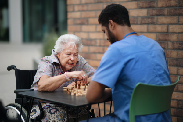 Caregiver playing chess with his client outdoor at a cafe.