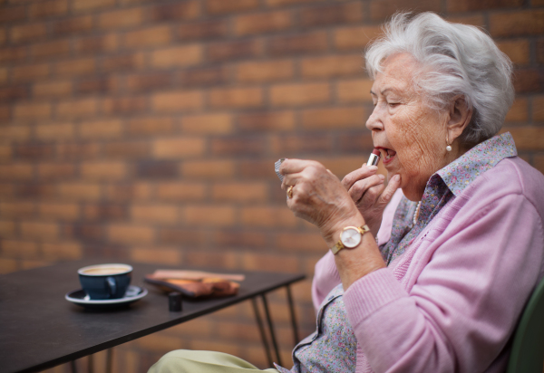 Happy senior woman putting a lipstick on her lips enjoying coffee in city.