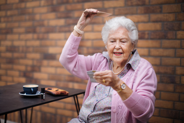 Happy senior woman combing her hair, enjoying a coffee in city.