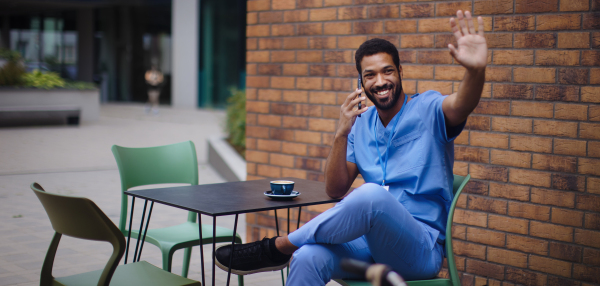 Nurse man sitting and waving for someone, outdoor at cafe.